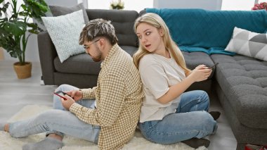 Bir çift oturma odalarında sırt sırta oturuyor, açıkça anlaşmazlık içindeler, ilişkilerinde gerginlik var..