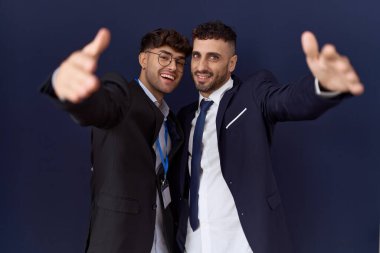 İki İspanyol iş adamı iş kıyafetleri içinde kameraya bakıp kucaklaşmak için gülümsüyor. Mutluluğu kucaklayan neşeli bir ifade.. 