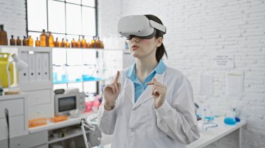 Modern bir laboratuvar ortamında sanal gerçeklik gözlüğü takan beyaz bir kadın, bilimde yenilikleri aktarıyor..