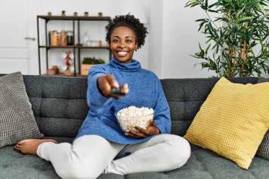 Afro-Amerikalı kadın evde kanepede oturmuş film izliyor.