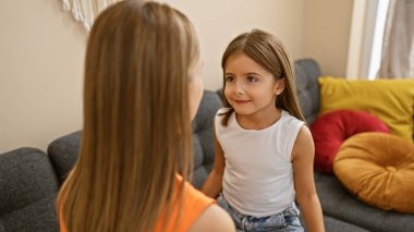 Genç bir kız ve kadın rahat bir oturma odasındaki kanepede yüz yüze oturur, aile ve beraberlik hissi uyandırır..