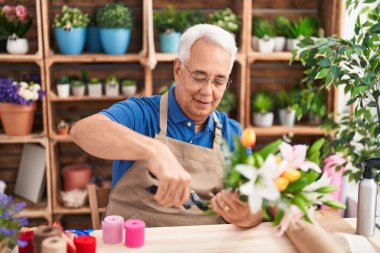 Orta yaşlı, kır saçlı bir çiçekçi çiçekçide çiçek buketi yapıyor.