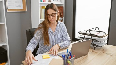 Gözlüklü odaklanmış bir kadın modern ofisinde profesyonellik ve konsantrasyonu anlatan belgeler inceliyor..
