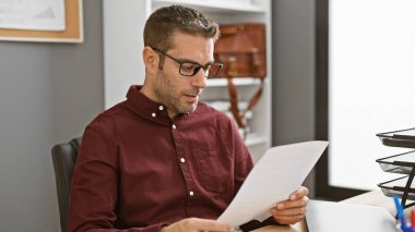 Modern ofis ortamında gözlüklü yakışıklı İspanyol bir adam okuyor.