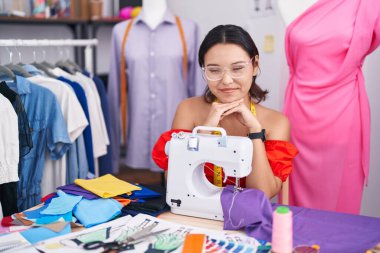 Dikiş makinesi kullanan İspanyol kadın terzi elleri çenesinde gergin ve heyecanlı bir şekilde yan tarafa bakıyor. 