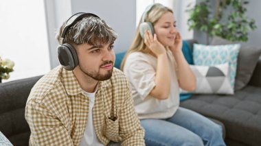 Bir erkek ve kadın rahat bir oturma odasında kanepede oturup kulaklıklarla müzik dinliyorlar.