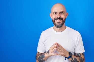 Mavi arka planda dövmeleri olan İspanyol bir adam el ele tutuşup gülümseyerek gevşemiş ve neşeliydi. Başarı ve iyimserlik 