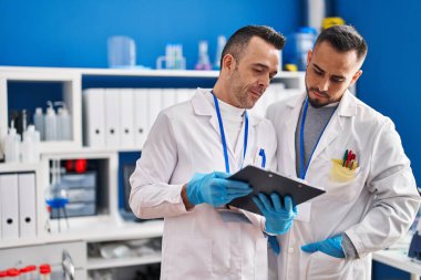 Two men scientists reading document with relaxed expression at laboratory