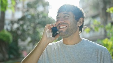 Yakışıklı, genç bir adam, kendine güvenen bir gülümsemesi olan, akıllı telefonuyla komik bir sohbetten hoşlanan. Sarışın, sakallı bir adamın açık hava portresi. Yeşil bir şehir parkında telefonla konuşuyor..