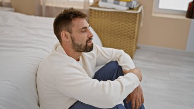 Stresli, genç, İspanyol bir adam, tamamen uyanık, evde tek başına oturuyor, baş ağrısı çekiyor. pijamalı depresif bir adam, battaniyenin altında, endişeli ve endişeli bir ifade.