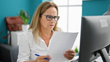 Ofisteki bilgisayar okuma belgesini kullanan orta yaşlı İspanyol iş kadını.