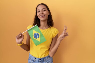 Brezilya bayrağı tutan genç İspanyol kadın kameraya gülümseyen ve parmaklarıyla zafer işareti yapan. İki numara.. 