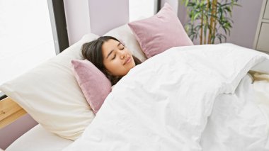 Genç bir İspanyol kadın, beyaz ve pembe yastıklarla aydınlık bir yatak odasında huzur içinde uyuyor..