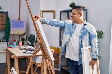 Genç Latin sanatçı gülümsüyor. Sanat stüdyosuna özgüvenli bakıyor.