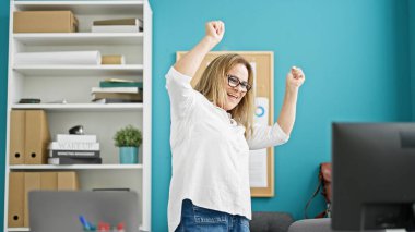 Orta yaşlı İspanyol iş kadını ofiste bilgisayar kullanarak kutlama yapıyor.