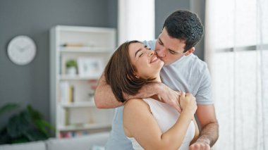 Güzel bir çift ayakta birbirlerine sarılıp evde öpüşüyorlar.