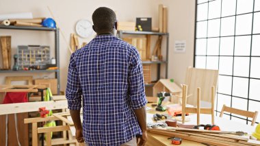 Marangozluk atölyesinde çalışan Afro-Amerikan bir adam içeride marangozluk aletlerine bakıyor.