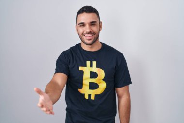 Bitcoin tişörtü giyen genç İspanyol adam gülümsüyor. Avuç içi dolusu yardım eli uzatıyor ve kabul ediyor.. 