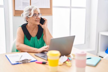 Orta yaşlı, kır saçlı, iş kadını. Ofiste bilgisayarla konuşuyor.