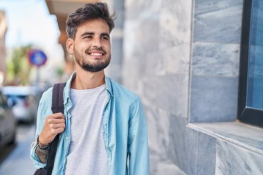 Young hispanic man student smiling confident wearing backpack at street