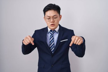 Genç Asyalı takım elbiseli ve kravatlı bir adam parmaklarını göstererek reklamını yapıyor, şaşırmış yüzünü ve ağzını açıyor. 