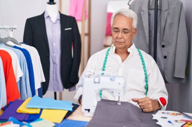 Gri saç terzisi olan orta yaşlı bir adam dikiş makinesi kullanıyor. Depresyonda ve endişe içinde, sinirli ve korkmuş. hüzünlü ifade. 