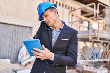 Young man architect talking on smartphone using touchpad at street