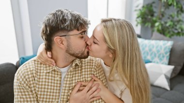 Sıcak bir oturma odasında bir erkeğin yanağını öpen bir kadın, aşkı ve yakın ilişkiyi simgeliyor..