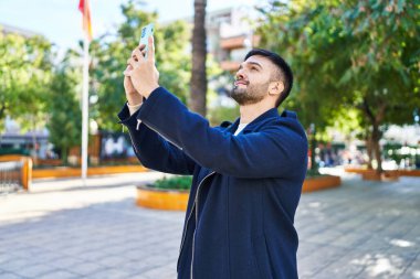 Young hispanic man smiling confident make photo by smartphone at park