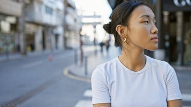 Güneşli bir şehir sokağında dalgın bir Asyalı kadının portresi.