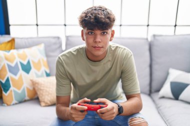 Young hispanic teenager playing video game sitting on sofa at home