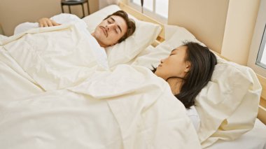 Irklar arası bir çift, rahat bir yatak odasında huzur içinde uyuyor. Bir erkek ve kadını evlerinde dinlenirken resmediyorlar..