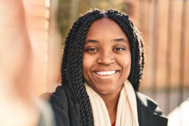Afro-Amerikalı kadın gülümsüyor. Sokakta kamerayla özçekim yapıyor.