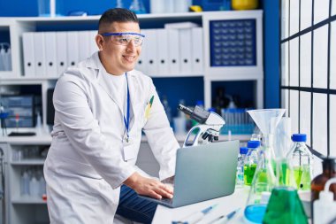 Laboratuvarda dizüstü bilgisayarını kullanarak gülümseyen genç Latin bilim adamı.