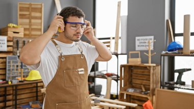 Sakallı bir zanaatkar, iyi organize edilmiş bir marangozluk stüdyosunda aletleri ve odunları ayarlıyor..
