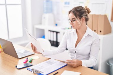 Genç sarışın iş kadını ofiste dizüstü bilgisayar okuyarak çalışıyor.