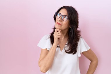 Orta yaşlı İspanyol kadın, günlük beyaz tişört ve gözlük takıyor kameraya kendinden emin bakıyor kolları çapraz ve çenesi açık gülümsüyor. Olumlu düşünmek. 