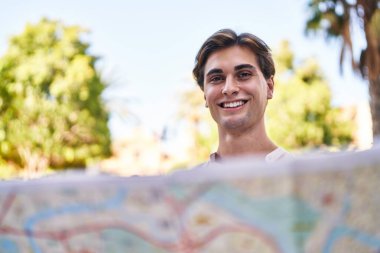 Young caucasian man smiling confident holding city map at park