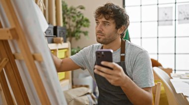 Mobil ekranına hevesle odaklanmış, kendine güvenen genç sakallı sanatçı, üniversite atölyesinin canlı sanat merkezindeki akıllı telefonuna titizlikle çiziyor.