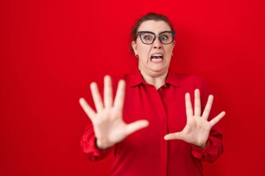 Kızıl arka planda kızıl saçlı genç bir İspanyol kadın korku ifadesinden korkuyor ve dehşete düşüyor. El kol hareketi yapmayı kes, şok içinde bağır. panik konsepti. 