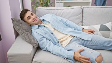 Mutlu erkek portresi, kendine güveni olan, yakışıklı İspanyol genç adam rahat rahat koltukta dinleniyor. Yüzünde neşe saçan bir gülümseme ile evin rahatlığıyla eğleniyor..