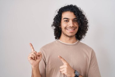 Beyaz arka planda duran kıvırcık saçlı İspanyol adam gülümsüyor ve kameraya bakıyor.. 