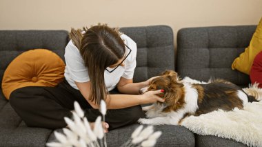 Latin bir kadın, rahat oturma odasında kanepede köpek besliyor. Şefkat ve arkadaşlık gösteriyor..