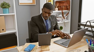 Modern ofiste dizüstü bilgisayarla çalışan, takım elbiseli, odaklanmış Afrikalı bir adam..