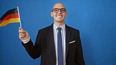 Genç İspanyol iş adamı elinde Alman bayrağı tutarken mavi arka planda gülümsüyor.