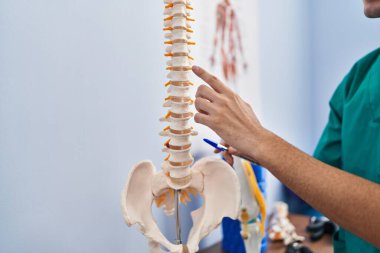 Young caucasian man physiotherapist touching anatomical model of spinal column at rehab clinic