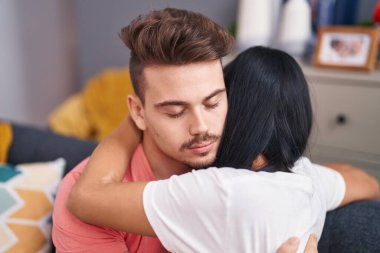 Erkek ve kadın çift evdeki kanepede oturup birbirlerine sarılıyorlar.