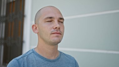 Genç İspanyol adam ciddi bir ifadeyle ayakta duruyor ve gözleri sokakta kapalı.