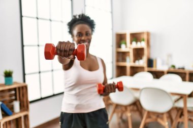 African american woman smiling confident using dumbbells boxing at home