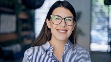 Ofiste kollarını kavuşturup gülümseyen gözlüklü güzel İspanyol kadın.